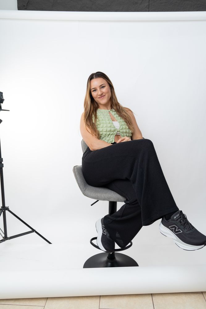 The photographer sitting on a stool in her studio, next to a light stand