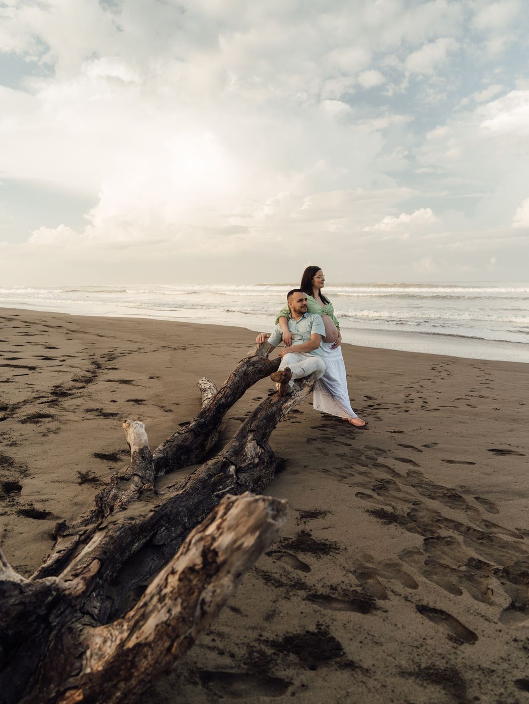 Couple sitting on driftwood on a beach at sunset
