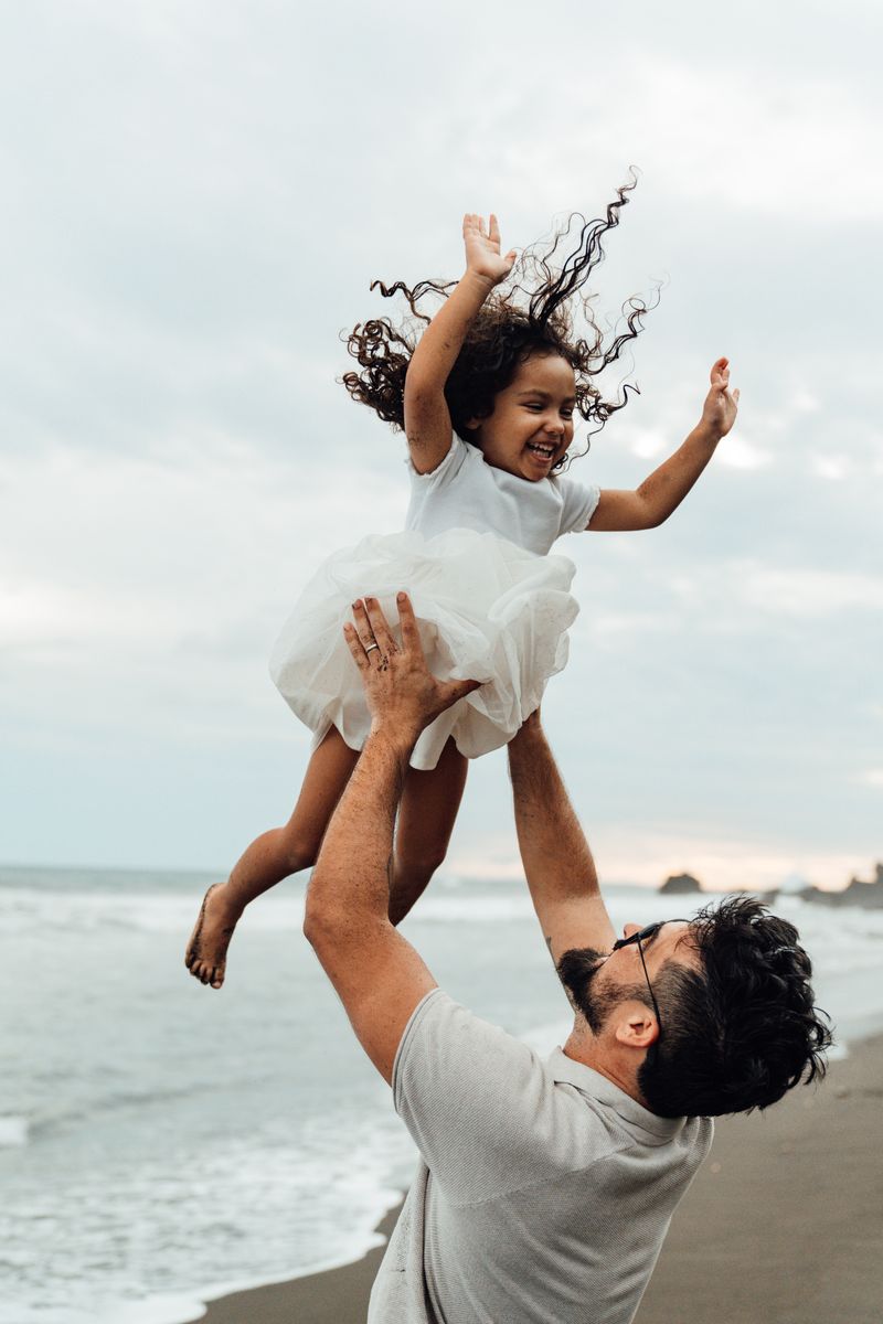 Father tossing his daughter in the air by the ocean